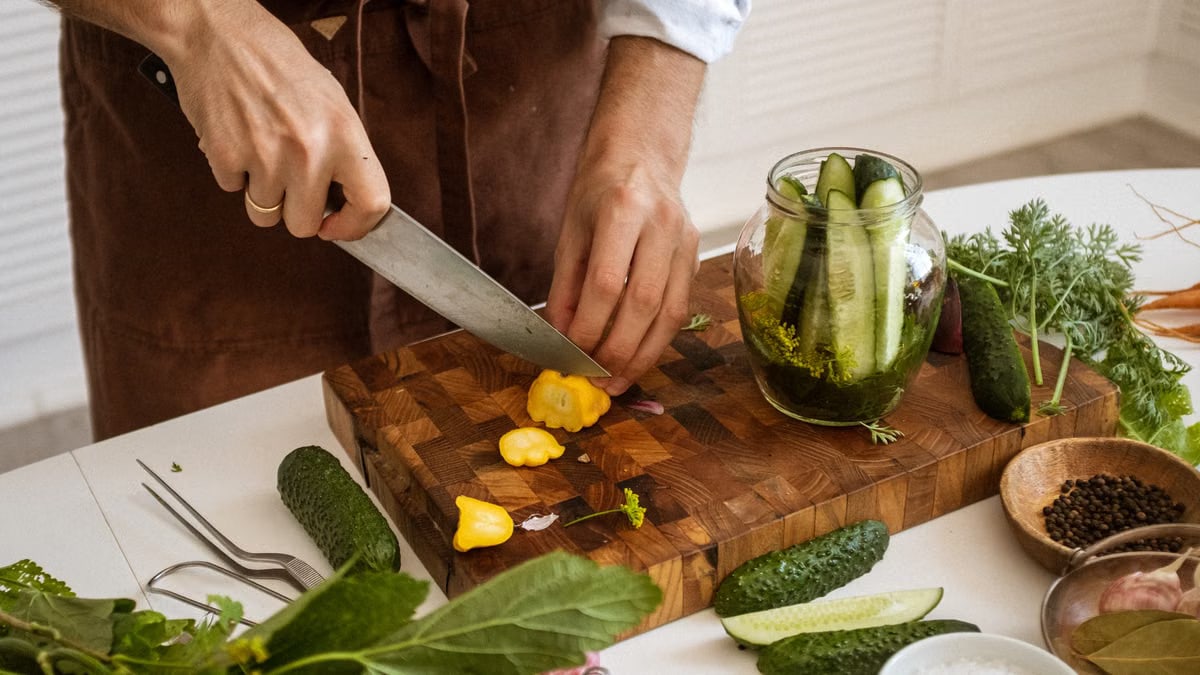 Person slicing vegetables on a wooden chopping board, showcasing fresh ingredients for a healthy meal.